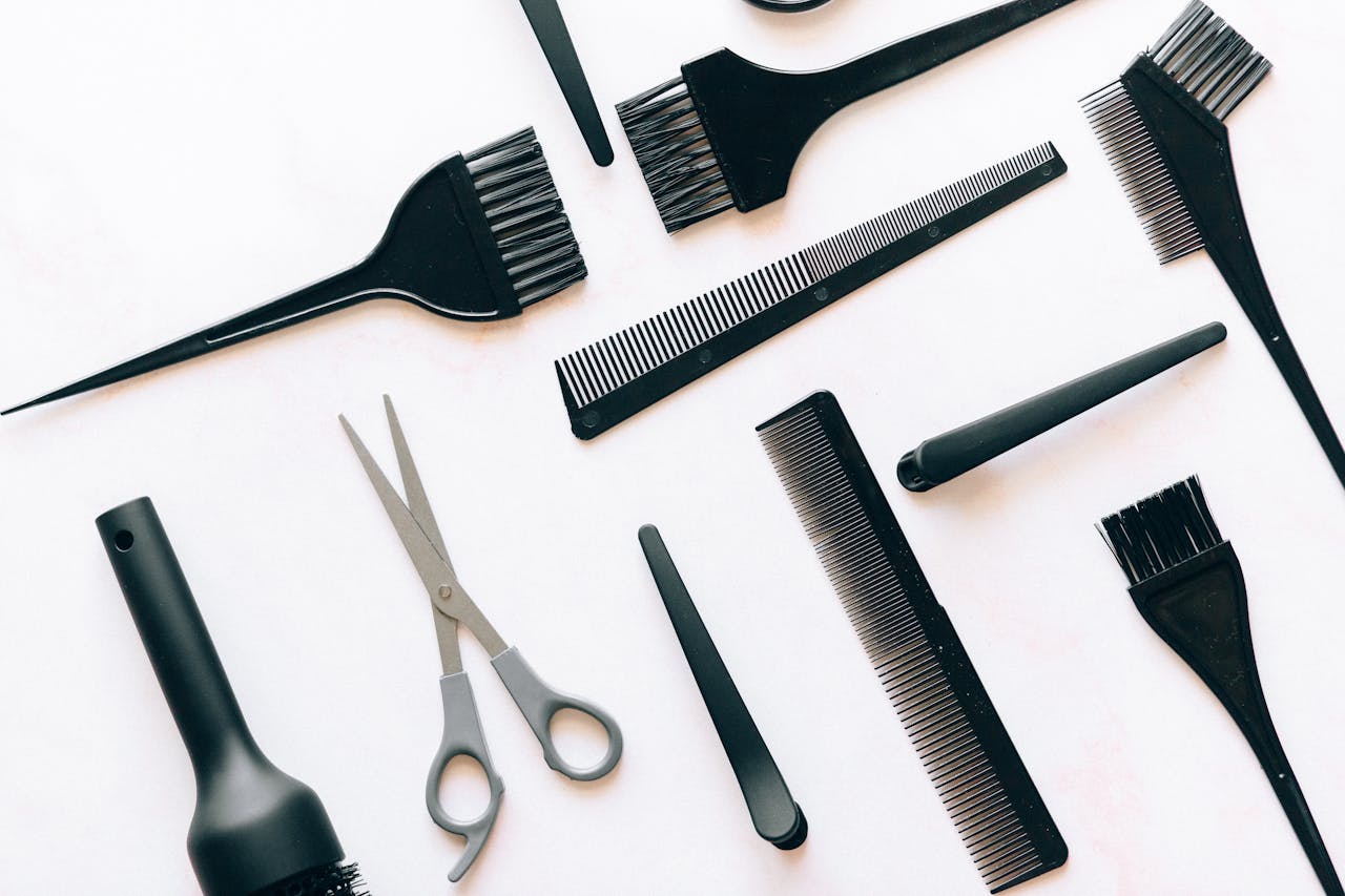 Flat lay of essential hairdressing tools including brushes, combs, and scissors on white background.